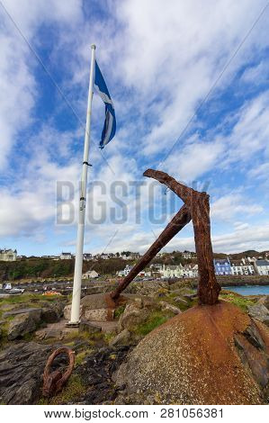 Scottish Flag On A White Flagpole And Rusty Boat Anchor In Portpatrick Harbor On An Overcast Day In 
