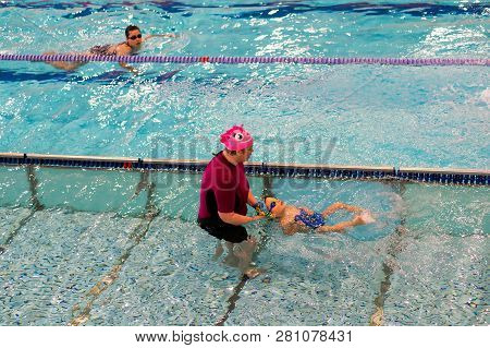 Poznan, Poland - January 26, 2019: Woman Assisting Boy Swimming On His Back In A Pool During Swim Le