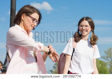 Mom And Teen Daughter Walking Along City Street. Mother Showing Her Daughter Clock On The Hand, Wome