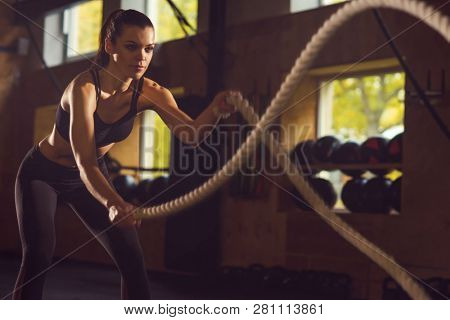 Fit, sporty and athletic sportswoman working in a gym. Woman training using battle ropes. Sports, athletics and fitness concept.
