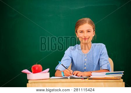 Back to school.. Funny beatifull girl sitting in the clasroom against blacboard. Child in school with book and accessories. Education concept