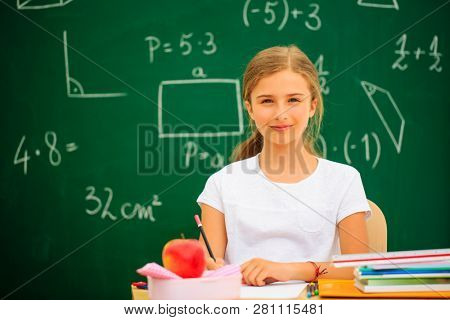 Back to school.. Funny beatifull girl sitting in the clasroom against blacboard. Child in school with book and accessories. Education concept