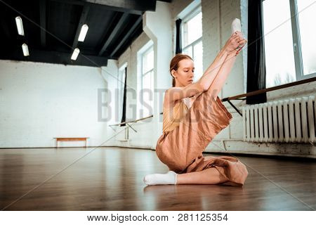 Cute Red-haired Teenager In Orange Pants Doing Legs Stretching