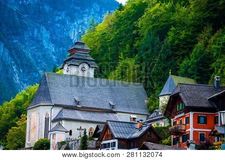 View of anient church and wooden houses at the green forest of mountain hill, in Hallstatt, Austria