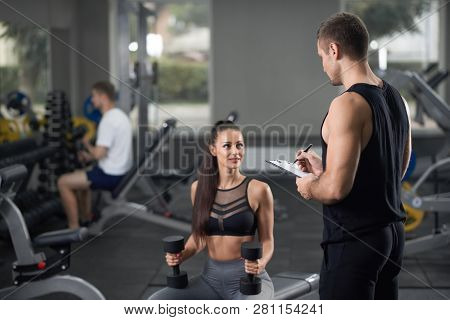 Heathy Fit Energetic Girl Training With Coach In Black Sportswear In Gym With Some Sports Equipment.