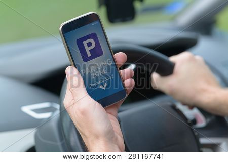 Driver using smartphone app to pay for parking in the paid parking zone in a city