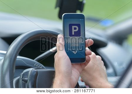 Driver using smartphone app to pay for parking in the paid parking zone in a city