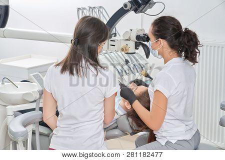 View From Back Of Female Dentists Working And Checking Teeth Of Female Patient In Dental Office. You