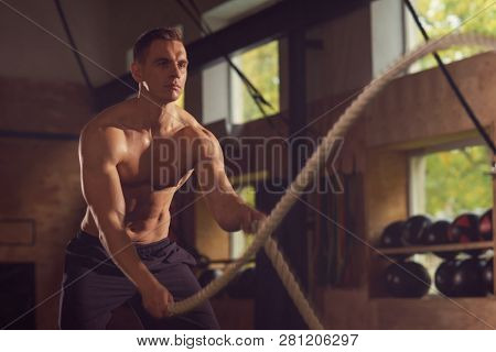 Fit, sporty and athletic sportsman working in a gym. Man training using battle ropes. Sports, athletics and fitness concept.