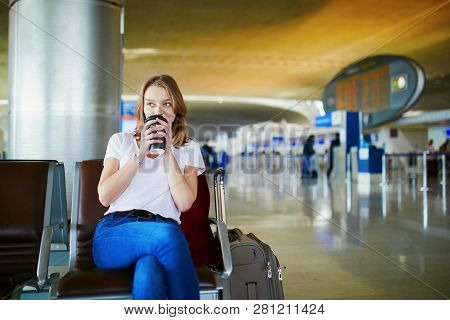 Young Woman In International Airport With Luggage And Coffee To Go, Waiting For Her Flight
