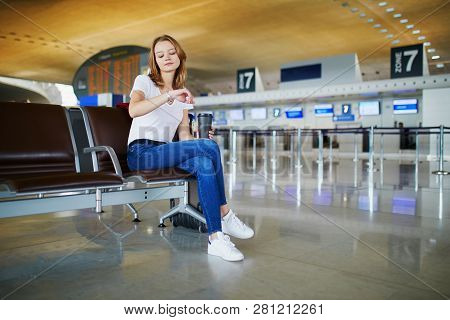 Young Woman In International Airport With Luggage And Coffee To Go, Waiting For Her Flight And Looki