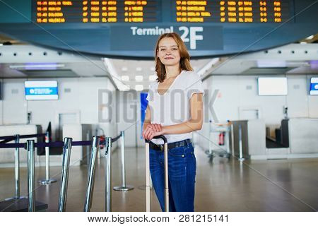 Young Woman In International Airport With Luggage Near Information Board Waiting For Her Flight