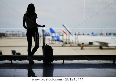 Silhouette Of Young Woman In International Airport, Looking Through The Window At Planes
