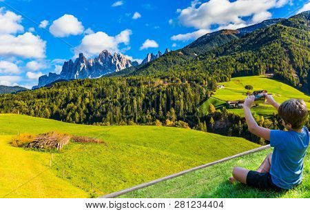 Charming boy in a blue T-shirt photographs the valley with a mobile phone. Beautiful landscape in the Dolomites. Wonderful day in South Tyrol. The concept of ecological and photo tourism