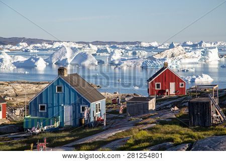 Rodebay, Greenland - July 09, 2018: Colorful Wooden Houses With Icebergs In The Background. Rodebay,