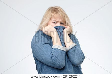 Blonde Girl In Blue Sweater Pulling Her Trendy Sweater Over Head.