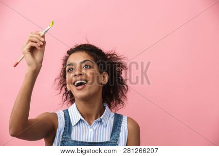 Beautiful young african woman atrist holding a paint brush over pink background