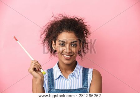 Beautiful young african woman atrist holding a paint brush over pink background