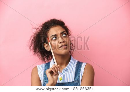 Beautiful young african woman atrist holding a paint brush over pink background