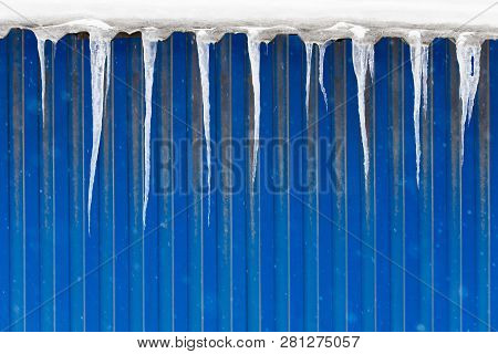 Roof Of Building With Blue Color Metal Wall Covered With Sharp Icicles. Ice Stalactite Hanging From 