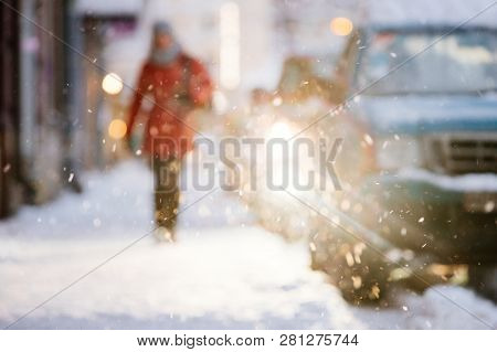 Defocused Abstract Blurred Image Of Female In Red Coat Walking Down The Street Along Parked Cars Dur