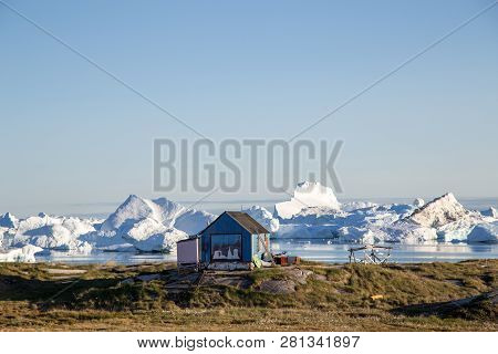 Rodebay, Greenland - July 09, 2018: A Blue Wooden House With Icebergs In The Background. Rodebay, Al