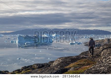 Rodebay, Greenland - July 09, 2018: A Man Is Walking And Looking At Icebergs. Rodebay, Also Known As