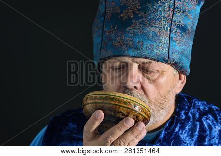 Nice Portrait Of Bearded Senior Man In Blue Oriental Clothes Drinking Tea From Piola