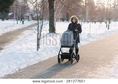 Beautiful Mother Walking In The Park With Her Little Baby In Stoller. Woman Dressed In Blue Jaket Wi