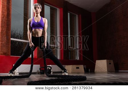 Fit And Muscular Woman Exercising With Battling Ropes At Fitness Studio. Female Athlete Doing Battle