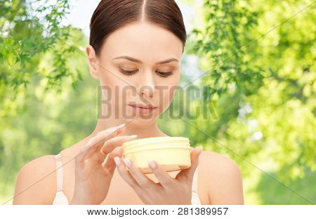 beauty and cosmetics concept - beautiful woman with moisturizing cream over green natural background