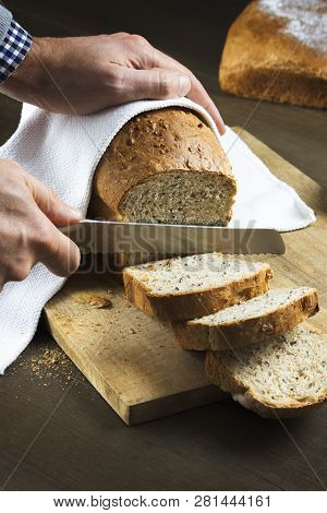 Whole Grain Bread Put On Kitchen Wood Plate. Hands Cutting Bread With A Serrated Knife . Fresh Bread