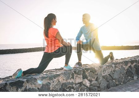 Young Health Couple Stretching Legs Next To The Beach At Sunset - Happy Sportive Lovers Workout Toge