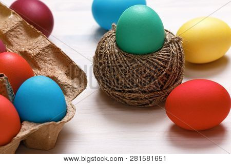 Easter Composition. Multi-colored Eggs In A Box, In A Nest Of Hemp Threads, On A White Table.