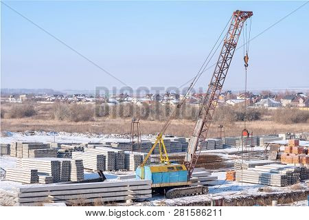 Crawler Crane, Piles And Concrete Slabs At A Construction Site Near A Multi-storey Building. Transla