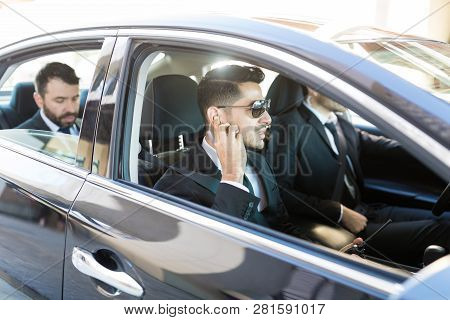 Young Bodyguard Listening To Earpiece While Sitting In Car With Vip