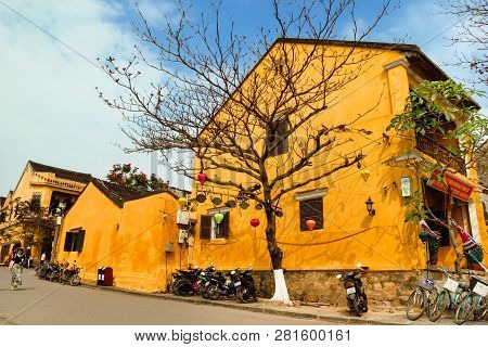 Hoi An, Vietnam - February 12, 2018: Touristic Street In Old Town With Yellow Houses, Big Tree, Moto
