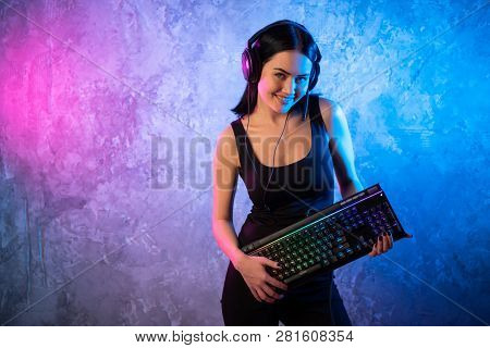Young Sexy Disco Girl Wearing Gaming Headset Holding Gaming Kyeboard. Room Lit In Retro, Retrowave O