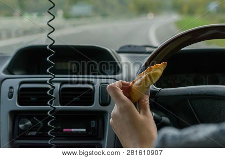 Closeup, Of Female Hand Holding A Bun Behind The Wheel Of The Car In Motion On Highway