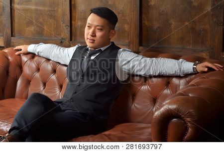 Successful Asian Man Sitting On A Leather Couch With His Hands Out To The Side