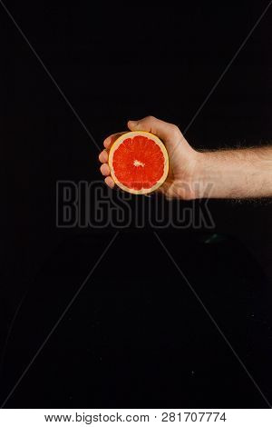 Half Of A Juicy Grapefruit In Man's Hand On Black Background