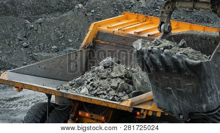 Excavator Fills Dump Truck. Bucket Excavator Closeup Loads Stones Into Body Of Dump Truck On Mining 