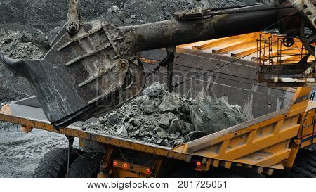 Excavator Fills Dump Truck. Bucket Excavator Closeup Loads Stones Into Body Of Dump Truck On Mining 
