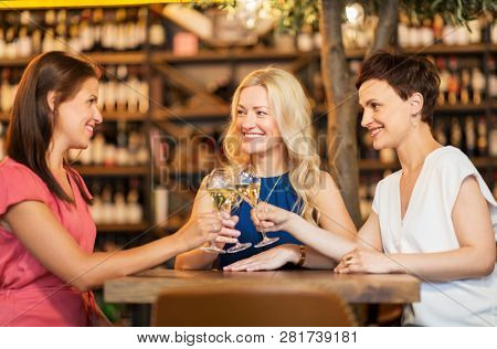 people, celebration and lifestyle concept - happy women drinking wine and clinking glasses at bar or restaurant