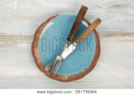 Top View Of Empty Blue Handmade Plate With Vintage Cutlery On A Grunge Background.