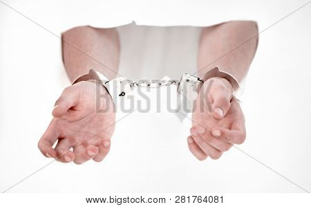Handcuffs on the hands of a man breaking a paper wall