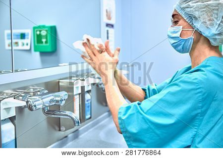 Female Surgeon In A Medical Mask And In A Suit In The Hospital Washing Thoroughly Her Hands Before P