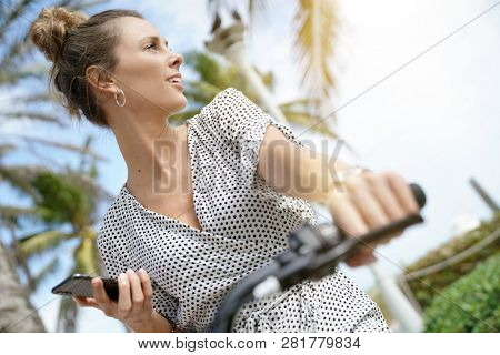 Pretty young woman sitting outdoors with bicylce and cellphone