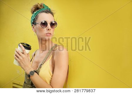 Styllish young woman with takeaway coffee outdoors on coloured background