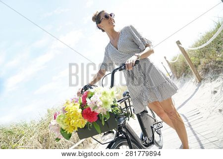 Gorgeous young woman in polka dot dress walking with bicylce on beach